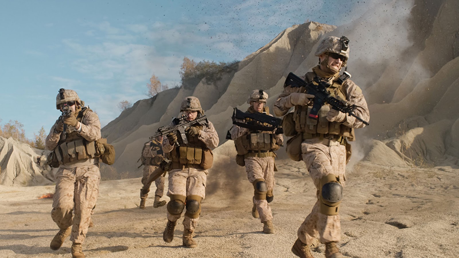 Soldiers in desert camouflage run through a rocky landscape, guns drawn. Dust rises around them, creating a tense and dynamic atmosphere under a clear sky.