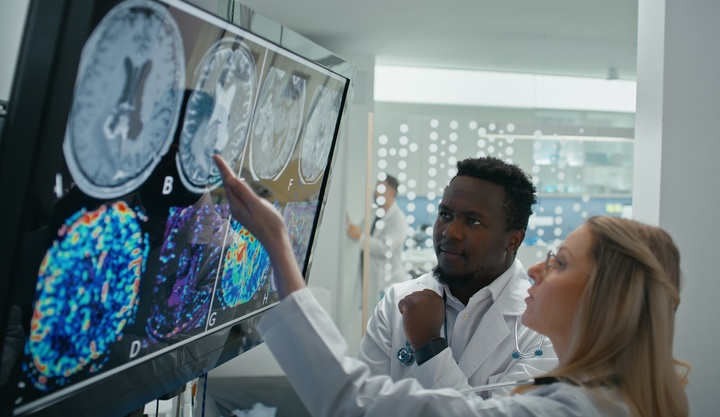 Two scientists in lab coats analyze brain scan images on a screen. One points at the display while the other observes thoughtfully, conveying focus.